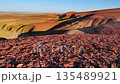 A desert, arid area subject to erosion against a backdrop of colorful hills. 135489921