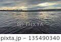Powerful ocean waves rolling toward shore near dark rocks at sunset with golden clouds on the horizon. Natural seascape background showing motion water energy and moody evening atmosphere. 135490340