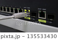 Hand plugging an Ethernet cable into a network switch port, showing wired internet connection, data transfer  135533430