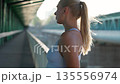 Woman runner rests on bridge over the river after morning jog, portrait of a sporty woman in slow motion, sportswoman after half-marathon training. 135556974