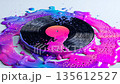 Glossy vinyl record melts into a pool of bright neon colors on a surface during a creative art process 135612527