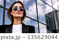 Confident businesswoman in sunglasses against modern glass building facade 135629044