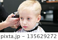Professional barber giving haircut to little blond boy 135629272