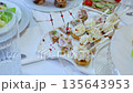 Herring canape topped with cream cheese, dill, red peppercorns resting on white plate amid festive holiday table setting with surrounding culinary elements 135643953