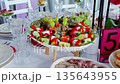 Vibrant vegetable skewers, sushi rolls, cheese cubes artfully arranged on white wooden legged platter, adorning elegant party spread 135643955