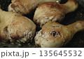 Chicken drumsticks are cooking in a pan. They sizzle in oil, reaching a golden brown hue under evening light in the kitchen. Smells of herbs and spices fill the air 135645532