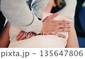 Close up of a practitioner's hands applying gentle pressure on a patient's torso during a hands-on therapy session 135647806