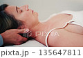 Side profile of a woman resting on a treatment table while a therapist supports her neck and head during a calm manual therapy session 135647811