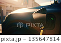Close up of an electric vehicle charging connector plugged into a car, with warm sunset light and lens flare 135647814