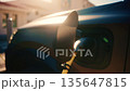 Close up of an electric vehicle charging connector plugged into a car, with warm sunset light and lens flare 135647815