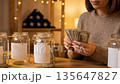 Woman counts us dollar bills and puts cash into glass jars with blank labels. Saving money concept perfect for veterans day budget or new year resolution financial goal. American flag background. 135647827