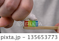 Hand holds bamboo toothbrush with rainbow bristles while applying white toothpaste 135653773