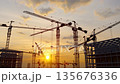 aerial view of tower cranes operating at a busy construction site under the setting sun 135676336