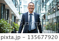 Middle-aged Asian HR manager walking confidently through modern office building with briefcase 135677920