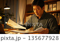 Middle-aged Asian HR manager reviewing documents in a cozy, warm-lit office 135677928