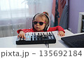 A young girl sits at a table at home crafting music on a midi keyboard. She has headphones on and is focused on her creative process. Her playful spirit shines through as she enjoys her hobby 135692184