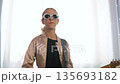A girl enjoys her time playing electric guitar at home while wearing sunglasses. She immerses herself in the music, showcasing her creative process and love for this hobby 135693182