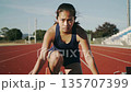 A female track and field athlete concentrates at the starting line and pushes off the ground with force. A female track and field athlete concentrates at the starting line and pushes off the ground with force. 135707399