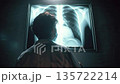 Doctor examining a glowing chest X-ray in a dark room for medical diagnosis. 135722214