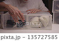 Close-up front view of young man organizing and storing seasonal shoes in clear plastic containers, keeping neatly arranged and tidy, promoting home clean-up and decluttering efforts, slow motion. 135727585
