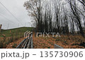 Narrow railway track running uphill through an autumn landscape with bare trees and fallen leaves 135730906