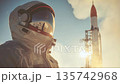 Astronaut prepares for launch at a space center with a towering rocket in the background during a bright morning 135742968