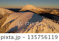 Cinematic aerial orbit view of golden sunrise over snowy mountain peaks. 135756119