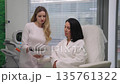 Professional aesthetician doctor consulting female client in modern cosmetology clinic, explaining procedure and showing information in document before beauty treatment. Shooting in slow motion. 135761322