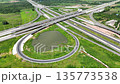 Aerial view of modern highway interchange with multilayer roads and curved ramps surrounded by green farmland, showcasing transportation infrastructure, urban development, and road network planning. 135773538
