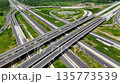 Aerial view of modern highway interchange with multilayer roads and curved ramps surrounded by green farmland, showcasing transportation infrastructure, urban development, and road network planning. 135773539