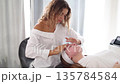 A beautician gently applies a face mask to a woman lying on a spa bed during a facial treatment. Calm atmosphere 135784584