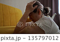 Woman On Sofa Shows Distress, Mature Woman Sits With Worried Expression, Depressed Woman Rests Her Head In Quiet Room, An Older Woman Appears Pained And Contemplative In Dimly Lit Space 135797012