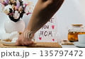 Female hands gently placing cookies and teapot with freshly brewed tea on table beside greeting card inscribed with I Love You Mom on a table with bouquet of flowers. Mothers Day concept 135797472