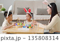 Easter family fun. A mother and child enjoy Easter traditions, painting colorful eggs with a paintbrush at home. A festive basket and decorations add joy to the holiday celebration. 135808314