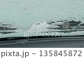 Wiper clearing ice patch on windshield leaving streaks and revealing partial view of wet road beyond 135845872