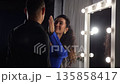 Dressing Room Mirror Woman Touches Partner Face Under Spotlight, Playful Flirtation, Dramatic Bulbs, Blue Dress, Warm Smiles, Gentle Caress, Intimate Backstage Atmosphere 135858417