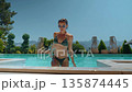 Fit young woman in bikini stepping out of the pool on a sunny summer day. Surrounded by greenery and 135874445