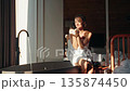 Playful young woman wrapped in a towel blows foam from her hands while enjoying a relaxing morning 135874450