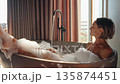Smiling woman enjoys a relaxing bubble bath in a modern freestanding tub inside a rustic wooden 135874451