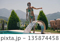 Athletic young woman in a bikini walking near a luxurious outdoor swimming pool on a sunny summer 135874458