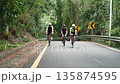 three young asian adults chatting while cycling on uphill rural road 135874595
