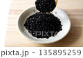 木のスプーンで小皿に黒胡麻を入れる 135895259