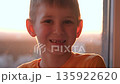 Child smiling funny. Joyful kid by sunny window at home. Young boy grinning in warm sunset light. Portrait little boy smile after falling out of his front baby teeth. 135922620