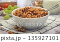 Bowl of granola on table with glass of milk, with fruits and nuts, slow motion 135927101