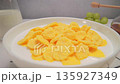 Bowl of corn flakes breakfast on marble kitchen table with glass of milk, fruits and nuts, slow motion, soft natural light and gentle shadows from window 135927349