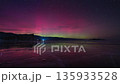 Red-green aurora borealis in the starry sky, reflected on the ice of the lake 135933528