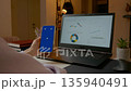 Businesswoman using smartphone with blue screen and laptop showing graphs 135940491
