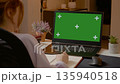 Working from home: A woman takes notes while using a green screen laptop 135940518