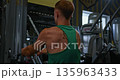 Back view of muscular man in green tank top doing triceps exercises on cable machine in gym. Fitness concept, healthy lifestyle, workout routine, strength training, gym equipment. 135963433