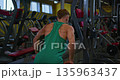 Back view of muscular man in green tank top training back muscles on cable machine in gym. He is building strength and endurance for fitness and healthy lifestyle. Gym interior background. 135963437